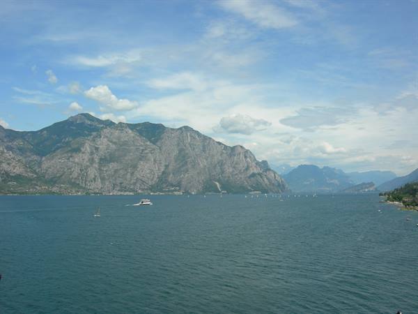 A ferry crosses the blue waters of Lake Garda between rocky mountains and clouds