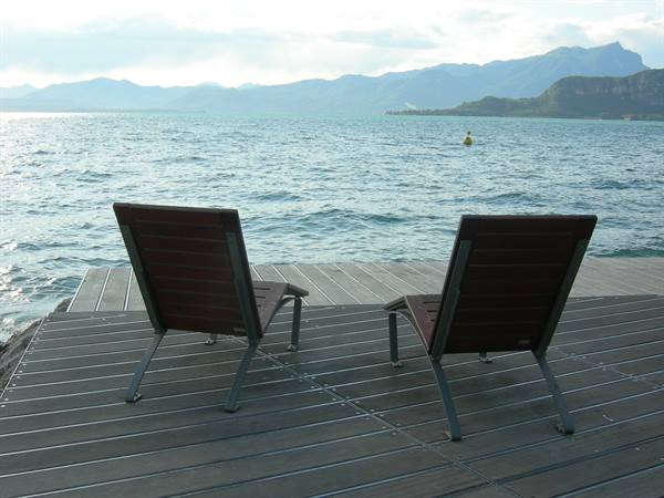 Two wooden deck chairs on a pier over Lake Garda