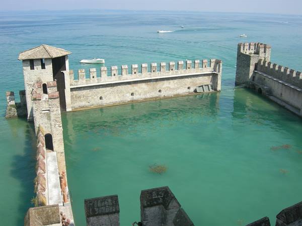 Crenellated walls of Scaligero Castle in Sirmione surrounded by turquoise Garda waters