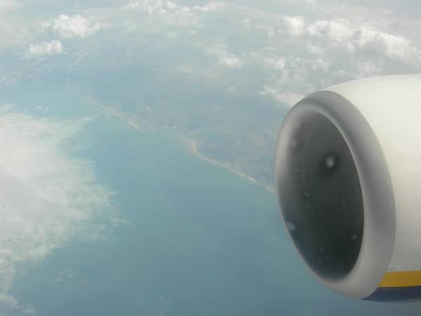 Airplane engine seen from the window above turquoise sea, coast and clouds