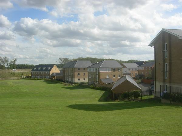New brick apartment buildings beside a wide green lawn, cloudy sky