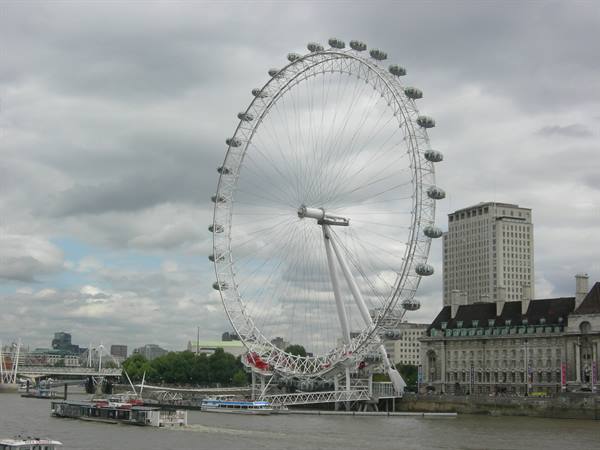 The London Eye ferris wheel above the Thames with boats passing by