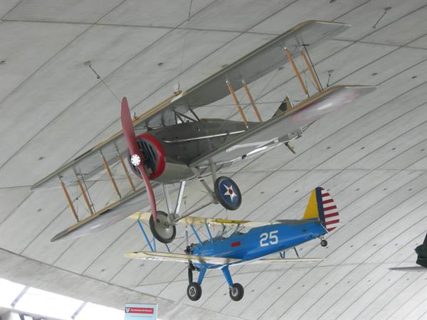 Two vintage biplanes suspended from the museum ceiling, one grey one blue