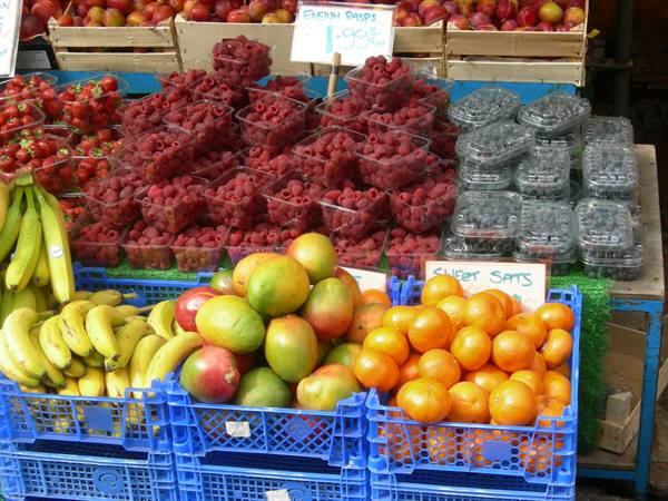 Market fruit stall with bananas, raspberries, blueberries, mangoes and satsumas in blue crates