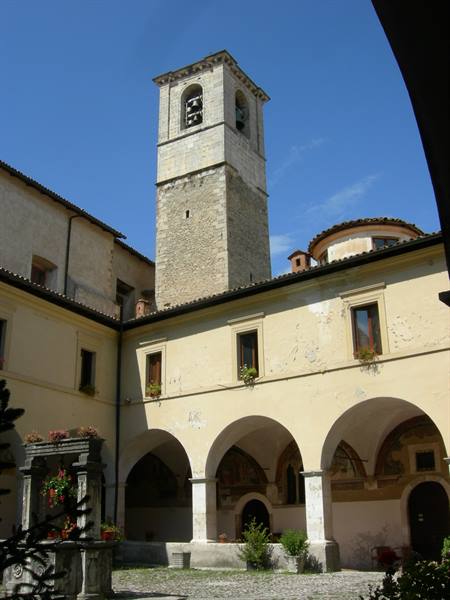 Cloister with arches and stone bell tower under blue sky