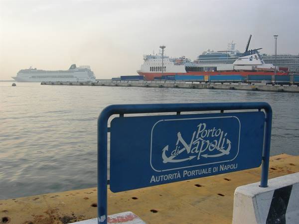 Blue Port of Naples sign on the dock, cruise ships moored in the haze