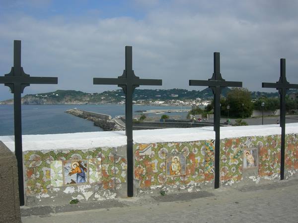 Iron crosses on tiled majolica wall, Ischia coastline in the background
