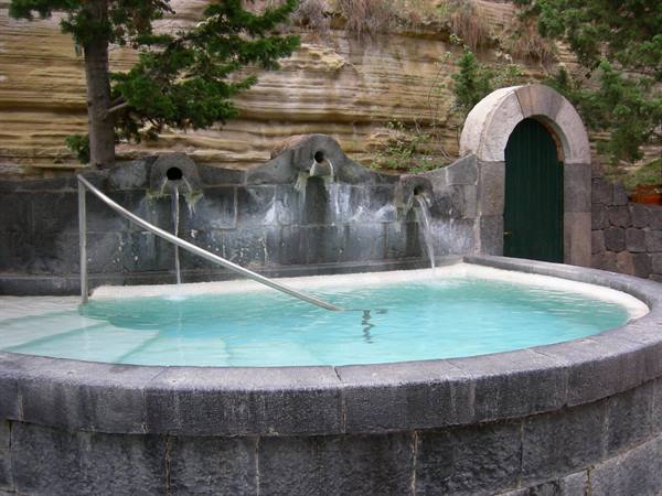 Round stone thermal pool with water spouting from carved spouts