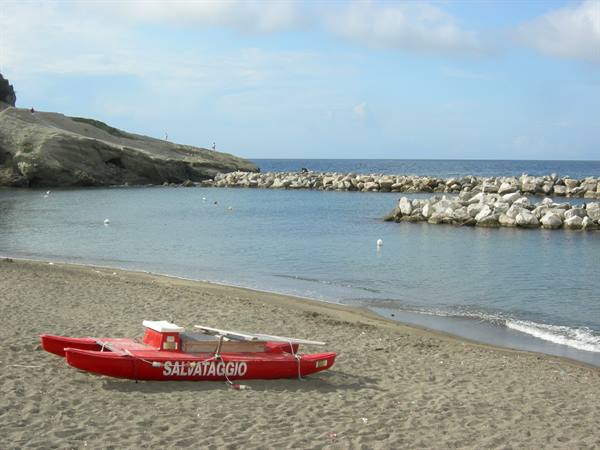 Red lifeguard boat on the sand in front of rocks and blue sea