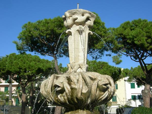 Limestone fountain with carved basin, water jets, pine trees and colorful houses