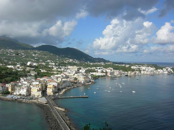 The bridge and bay of Ischia Ponte with boats and white houses under clouds