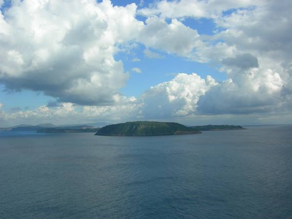 Green island in the blue sea under large white clouds