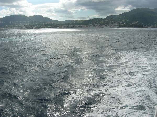 Boat wake foaming behind a moving vessel, green hills along the coast
