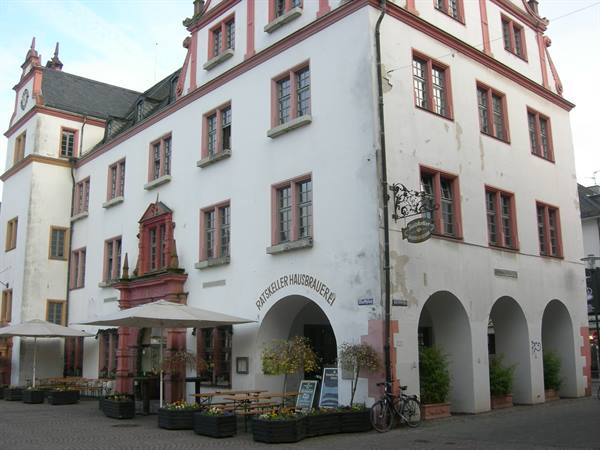 White palace with pink-framed windows and arcades, outdoor brewery with umbrellas in Coburg