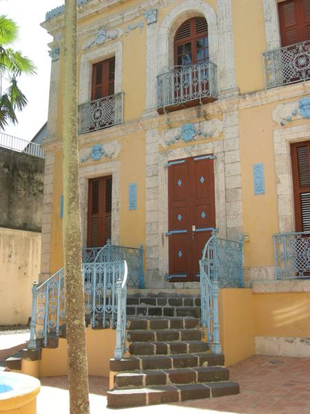 Dark stone steps leading to red door of yellow building with wrought-iron balconies