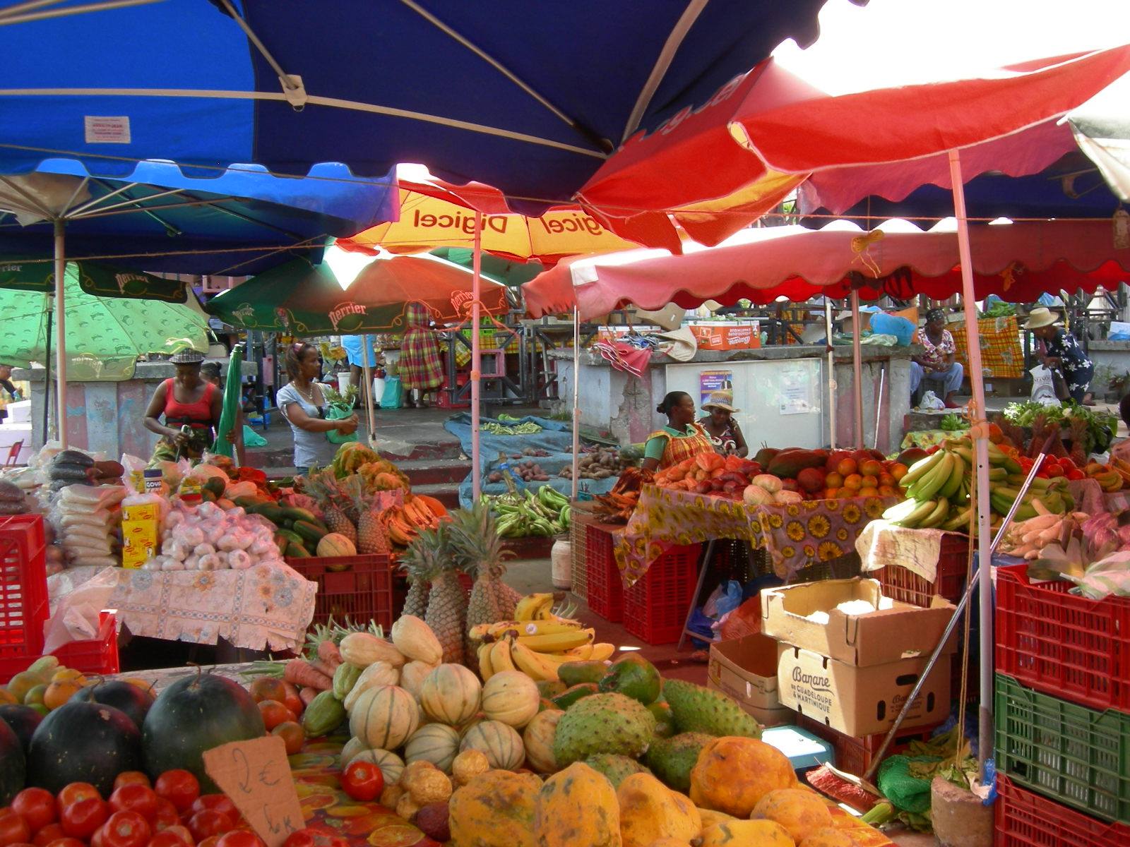 Open-air market under colorful umbrellas, bananas, pineapples and melons in plastic crates