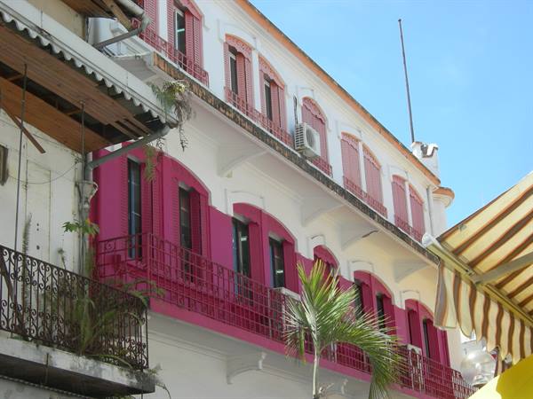 White and pink colonial building with wrought iron balconies and palm tree below
