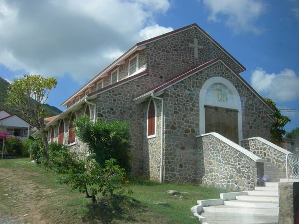 Stone church with white cross and staircase under a partly cloudy sky