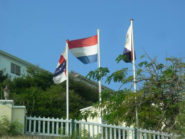 Dutch and Sint Maarten flags waving on white poles in front of a house