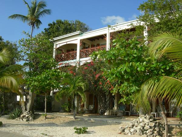 White hotel on sandy beach, palm trees and flowering bougainvillea under blue sky