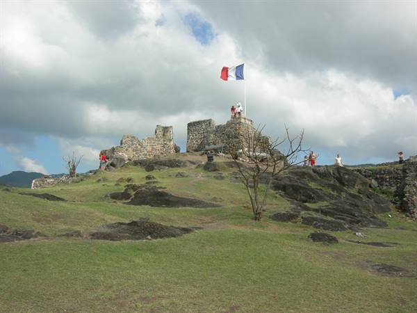 Tourists explore the stone ruins of Fort Louis under a French flag