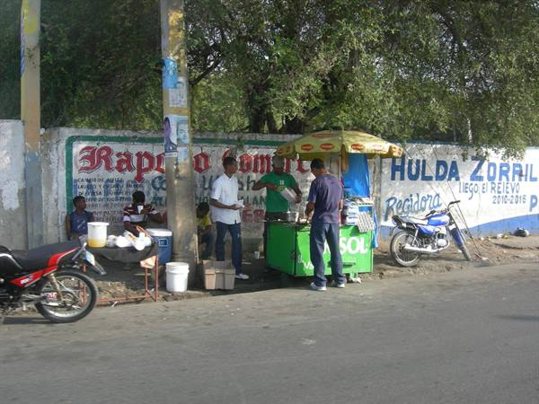 Street vendor at green cart under yellow umbrella, motorcycles parked nearby