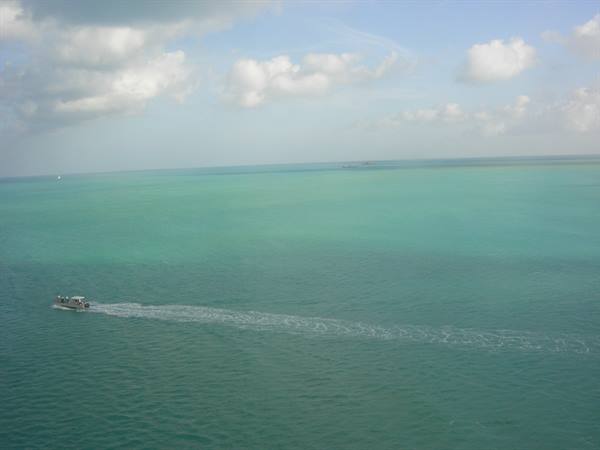 Small boat crossing turquoise sea under a cloudy sky