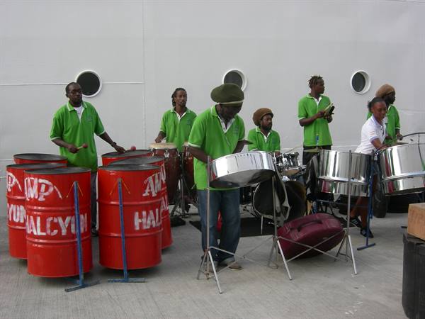 Musicians in green polos play steel drums and percussion in front of grey porthole wall