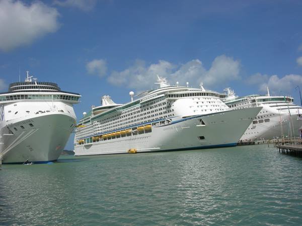 Three white cruise ships docked side by side in turquoise water under cloudy sky