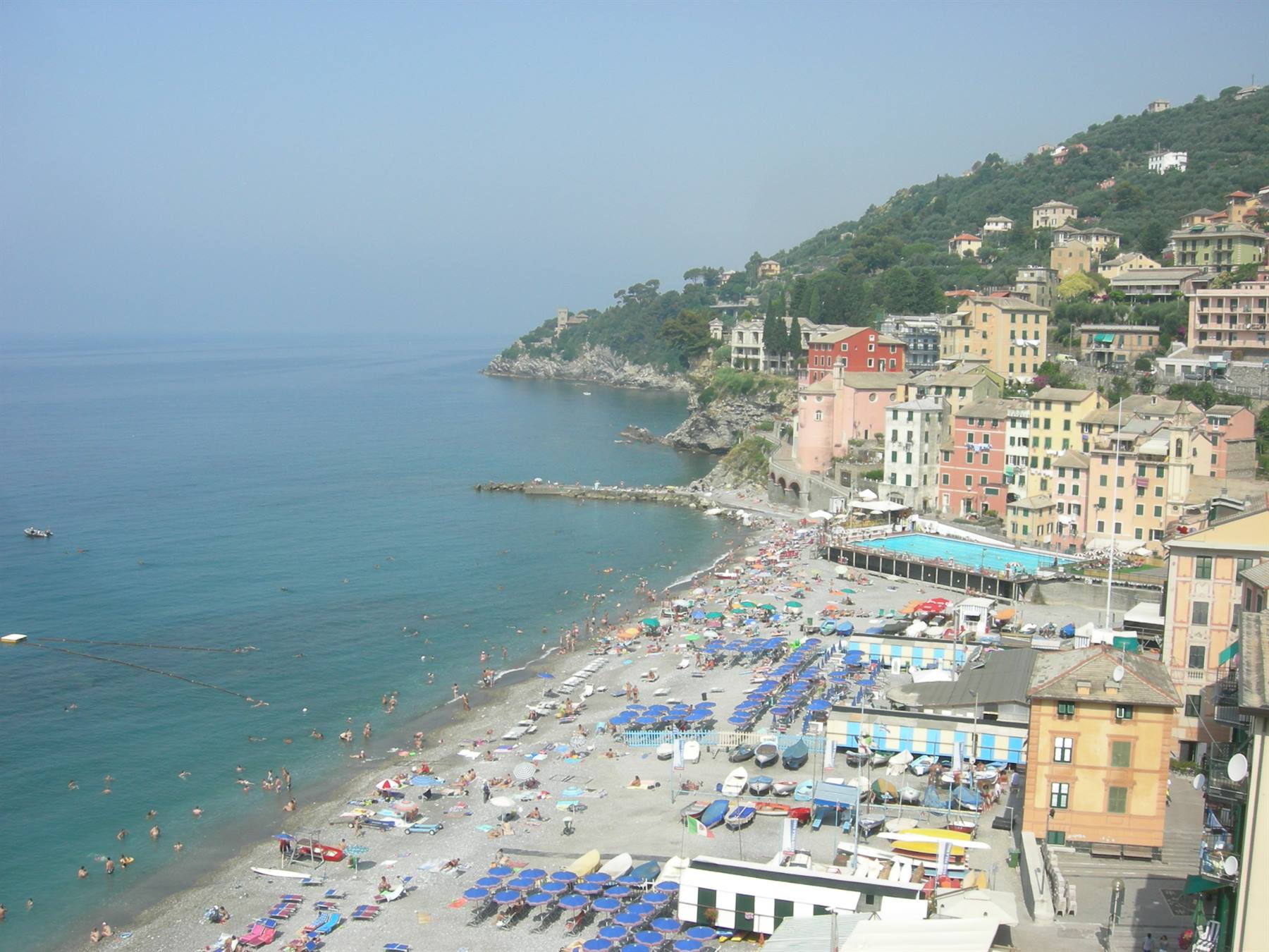 Crowded beach with blue umbrellas between colorful houses and turquoise sea