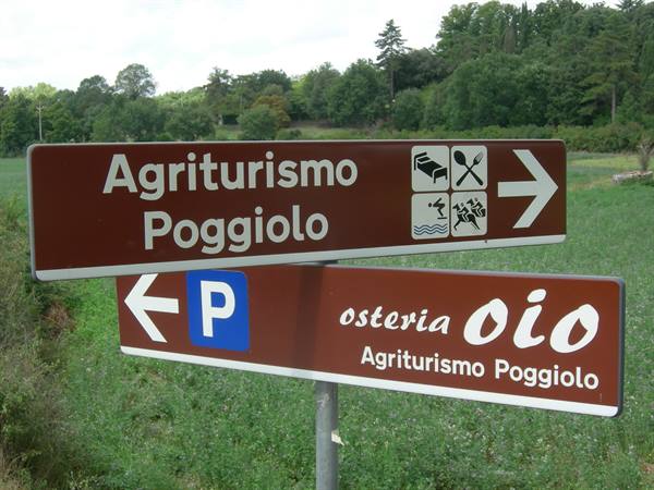 Brown signs point to Agriturismo Poggiolo and osteria Oio among green fields