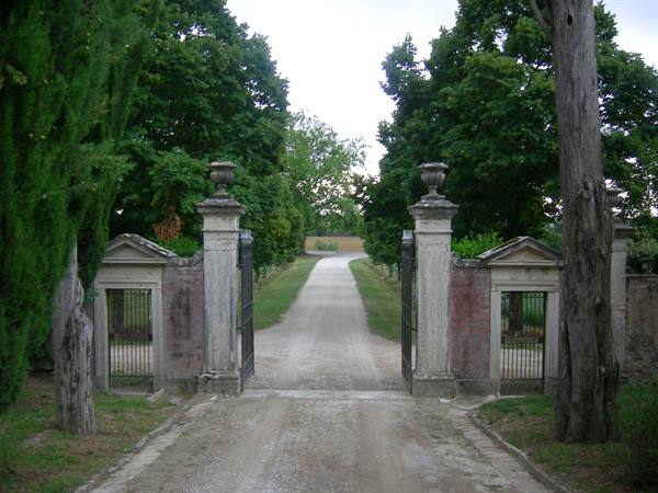 Stone gate with columns and urns, gravel road between green trees