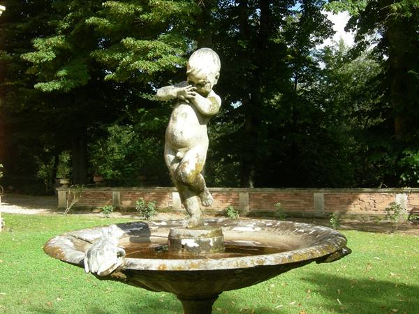 Stone cherub statue on garden fountain, brick wall and trees behind