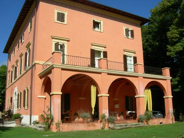 Pink villa with arches, wrought-iron balcony and yellow curtains, green lawn