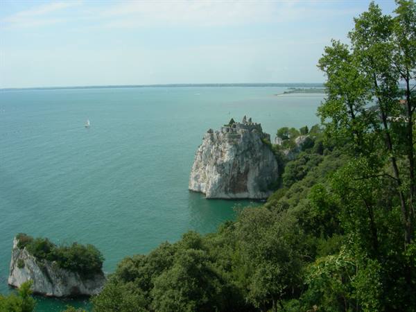 Duino Castle atop white cliff over green sea, trees in foreground