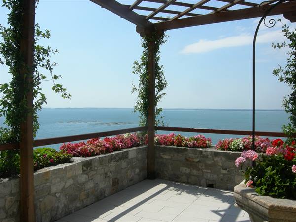 Wooden pergola with pink flowers on stone wall above the sea