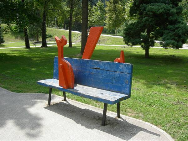 Blue wooden bench with orange sculptures in a green tree-lined park