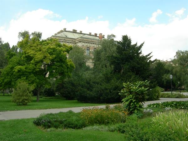 Public garden with flower beds, conifers and a historic green building among trees
