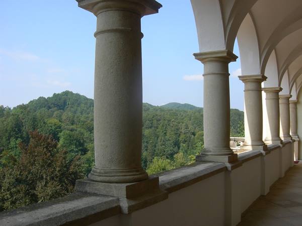 Stone colonnade with white arches overlooking forested hills in daylight