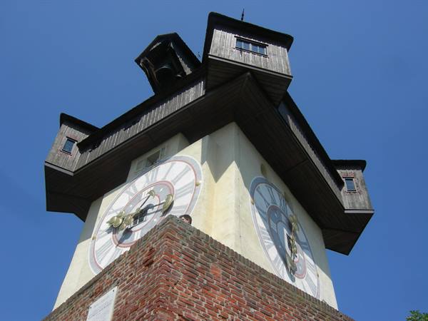 The clock tower of Graz, dark wood and two clock faces under blue sky