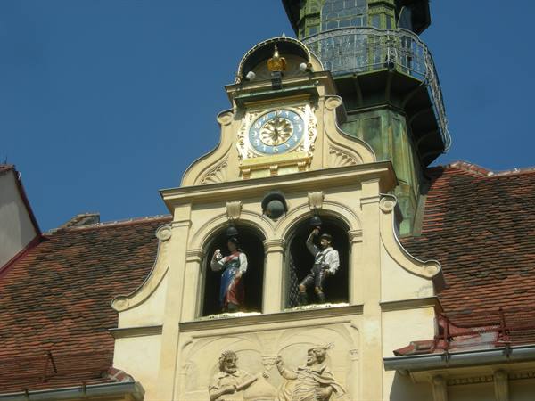 Gilded clock and moving figures in niches on historic facade, sunlight, blue sky