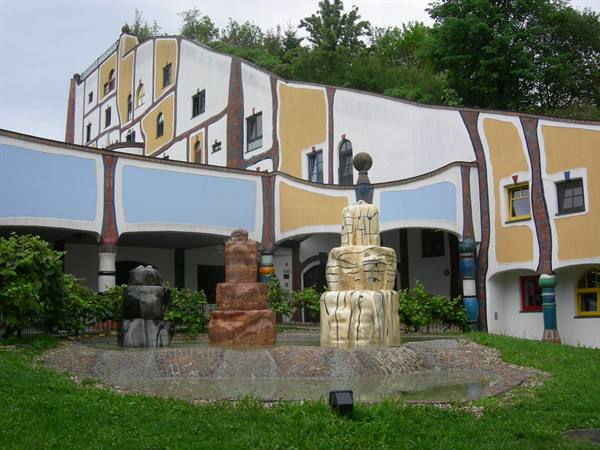 Curved colorful building with stacked stone fountains, soft overcast daylight