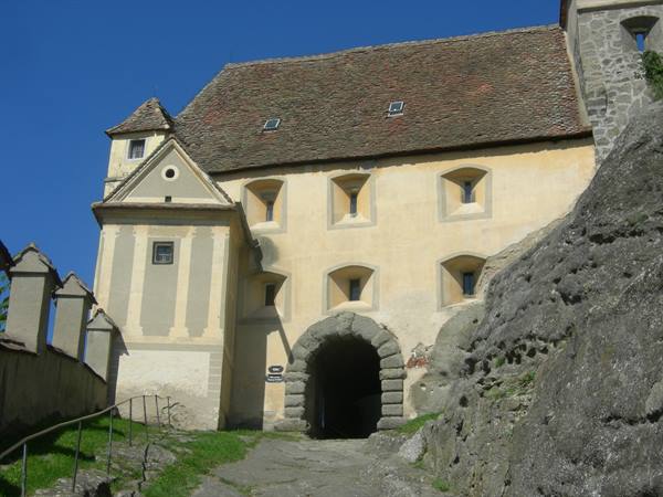 Yellow fortress facade with arched stone gate, rocks, clear blue sky, bright sunlight