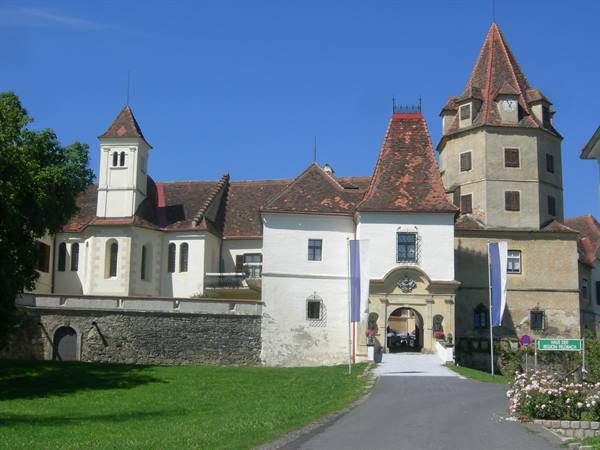 White castle with red conical towers under blue sky, paved road, sunlight