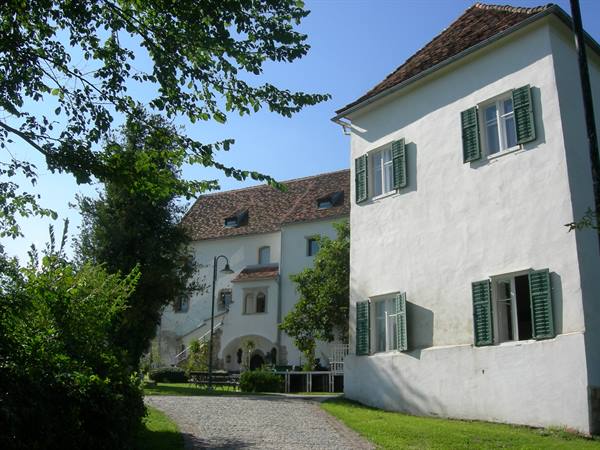 White house with green shutters along gravel path, sunlight, foliage, blue sky