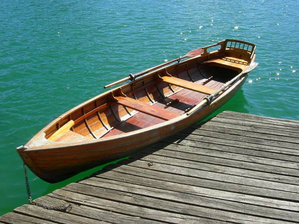 Wooden rowboat with oars tied to plank dock on green water