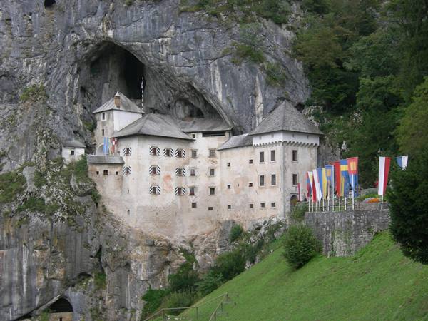 Predjama Castle built into the cliff face, colorful flags along the terrace