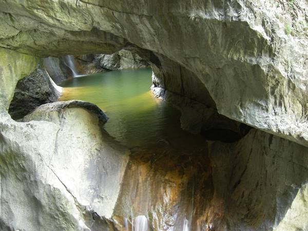 Waterfall flowing into a green pool framed by smooth rock