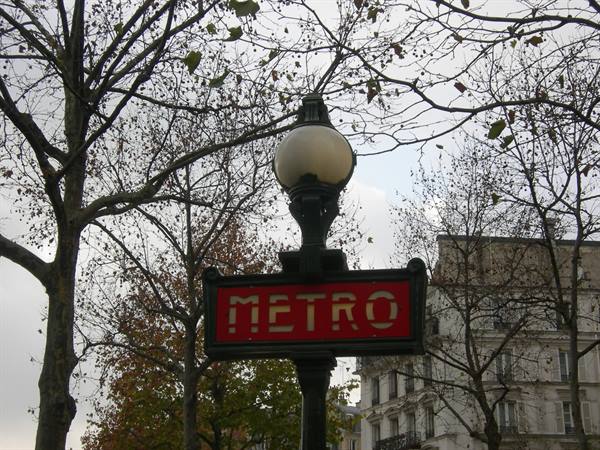 Red Paris metro sign among bare branches and grey sky