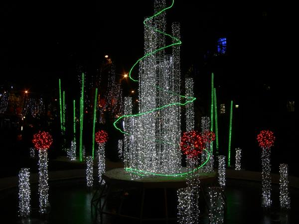 Christmas light installation with white towers, green spiral and red spheres at night